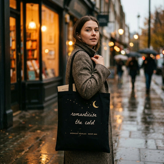 Woman carrying the black Romanticise the Cold tote bag outside a bookshop on a rainy autumn street