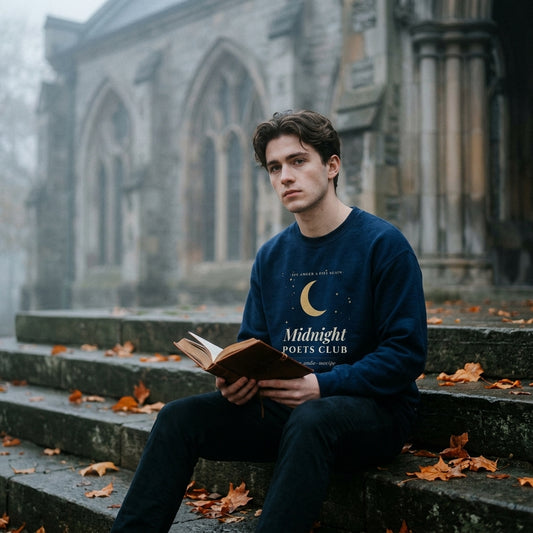 Man wearing the navy Midnight Poets Club sweatshirt reading poetry on gothic library steps in autumn